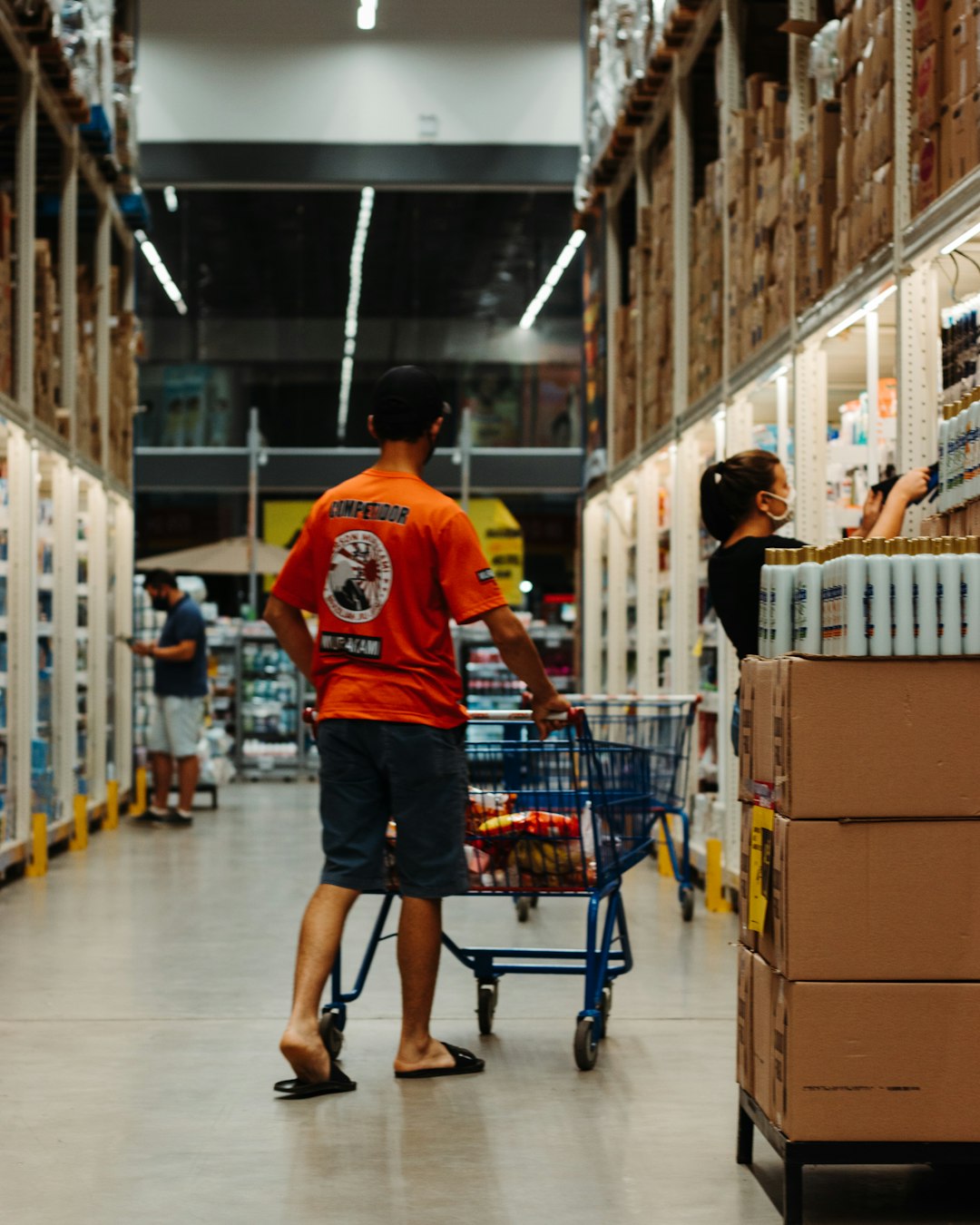 People walking buying things supermarket aisle by Perfume Brands man in red crew neck t-shirt and blue denim shorts standing beside shopping cart