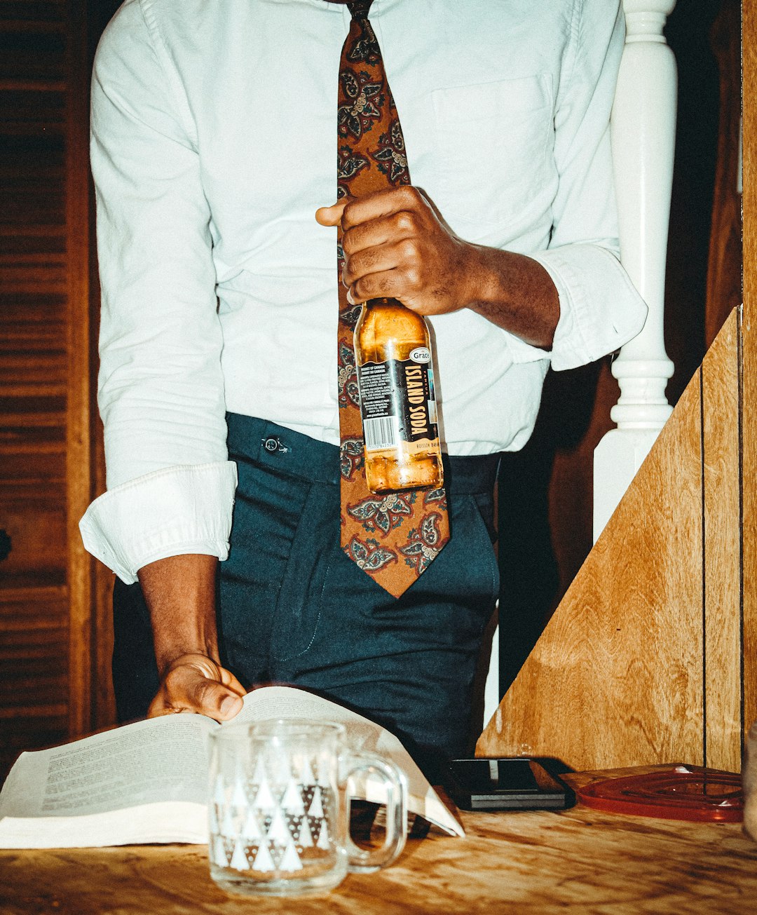 Man with a drink reading a book by Perfume Brands man in white long sleeve shirt holding brown glass bottle
